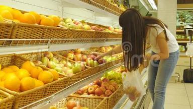 女人在杂货店挑选新鲜的红<strong>苹果</strong>，然后把它放进塑料袋里。 年轻漂亮的女孩
